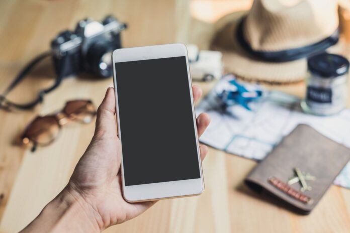 Hand holding a smartphone with travel accessories like passport and camera, planning a trip with apps